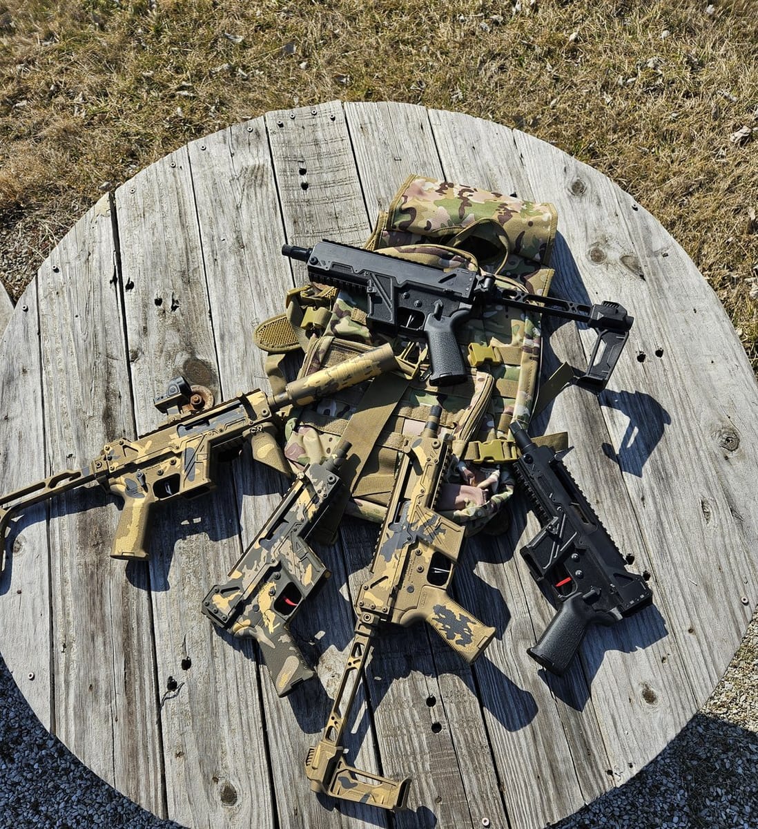 Several custom camo Cerakote firearms laid out with tactical gear